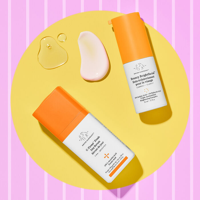 Bouncy Brightfacial et C-Firma Fresh à plat sur un fond rayé jaune et rose texturé à côté de produits