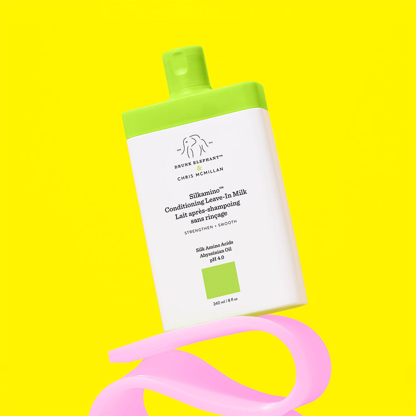 Lait revitalisant sans rinçage Silkamino sur un accessoire rose et un fond jaune.