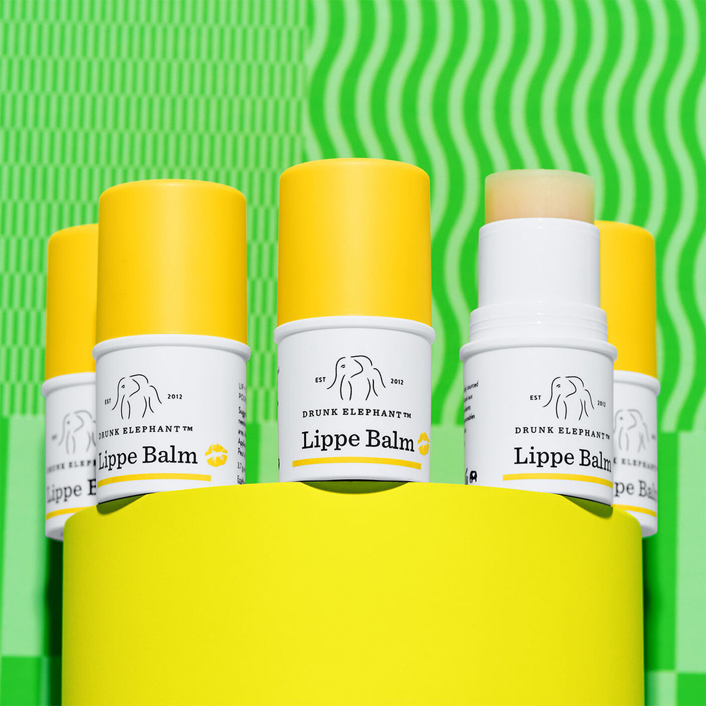 Lippe Balms circling on a yellow prop with one with the cap off showing the balm.